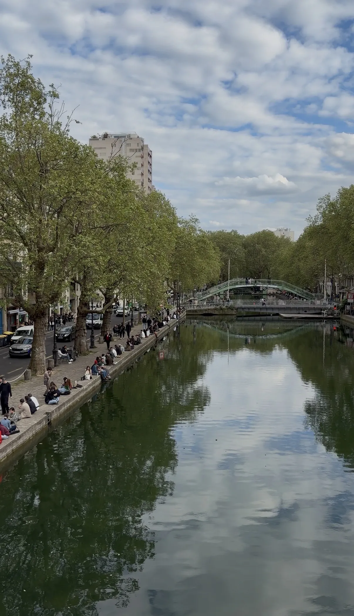 View looking down the Canal Saint-Martin in Paris. People sitting on both sides right beside the water.