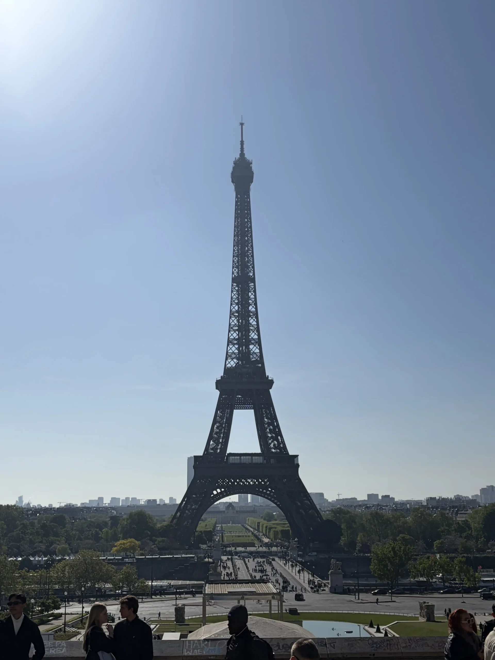 View of the iconic iron Eiffel Tower silhouetted against a bright, clear blue sky, as seen from the elevated Trocadéro terrace in Paris with visitors in the foreground.