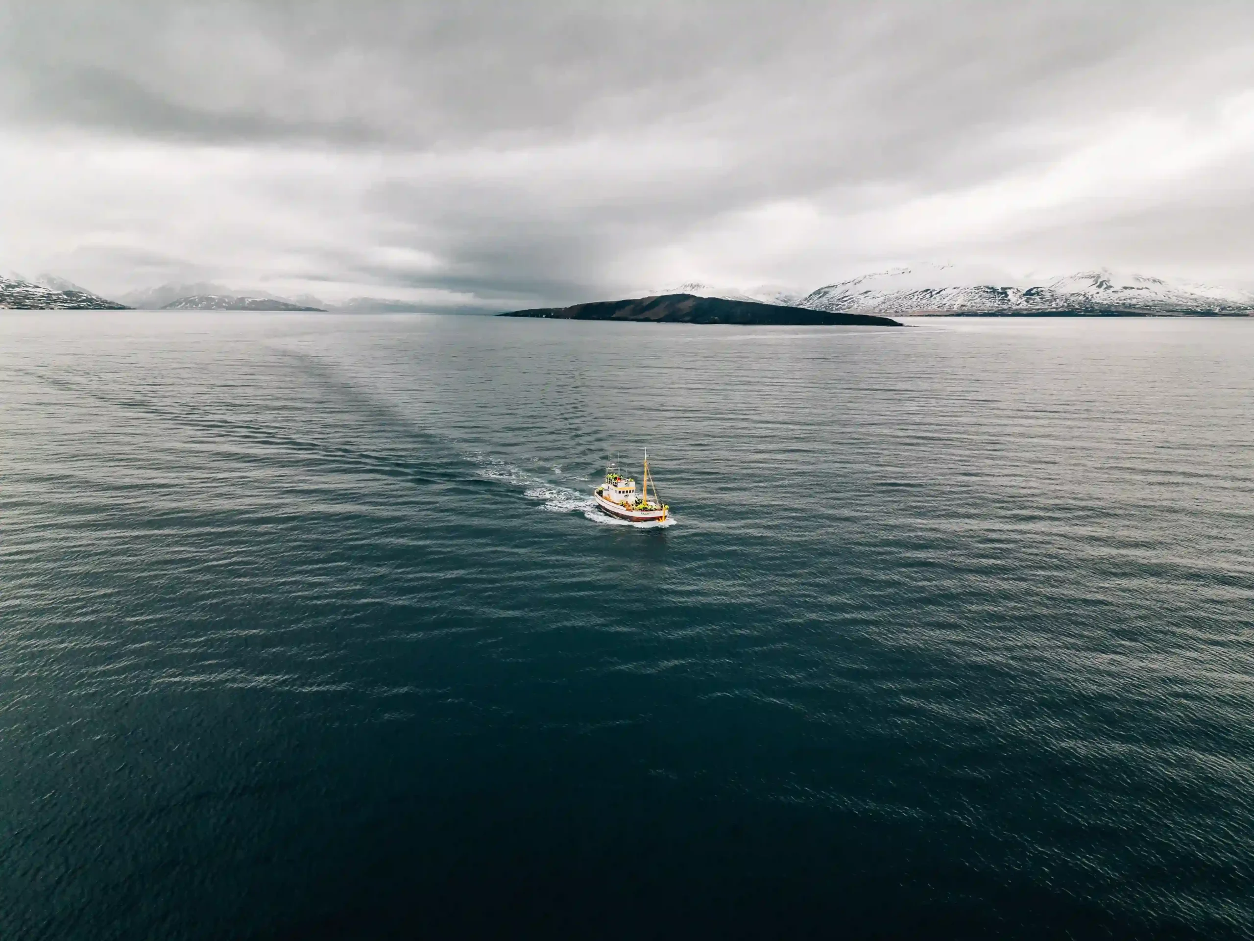 View of a small white and red boat cruising through dark, calm ocean waters.