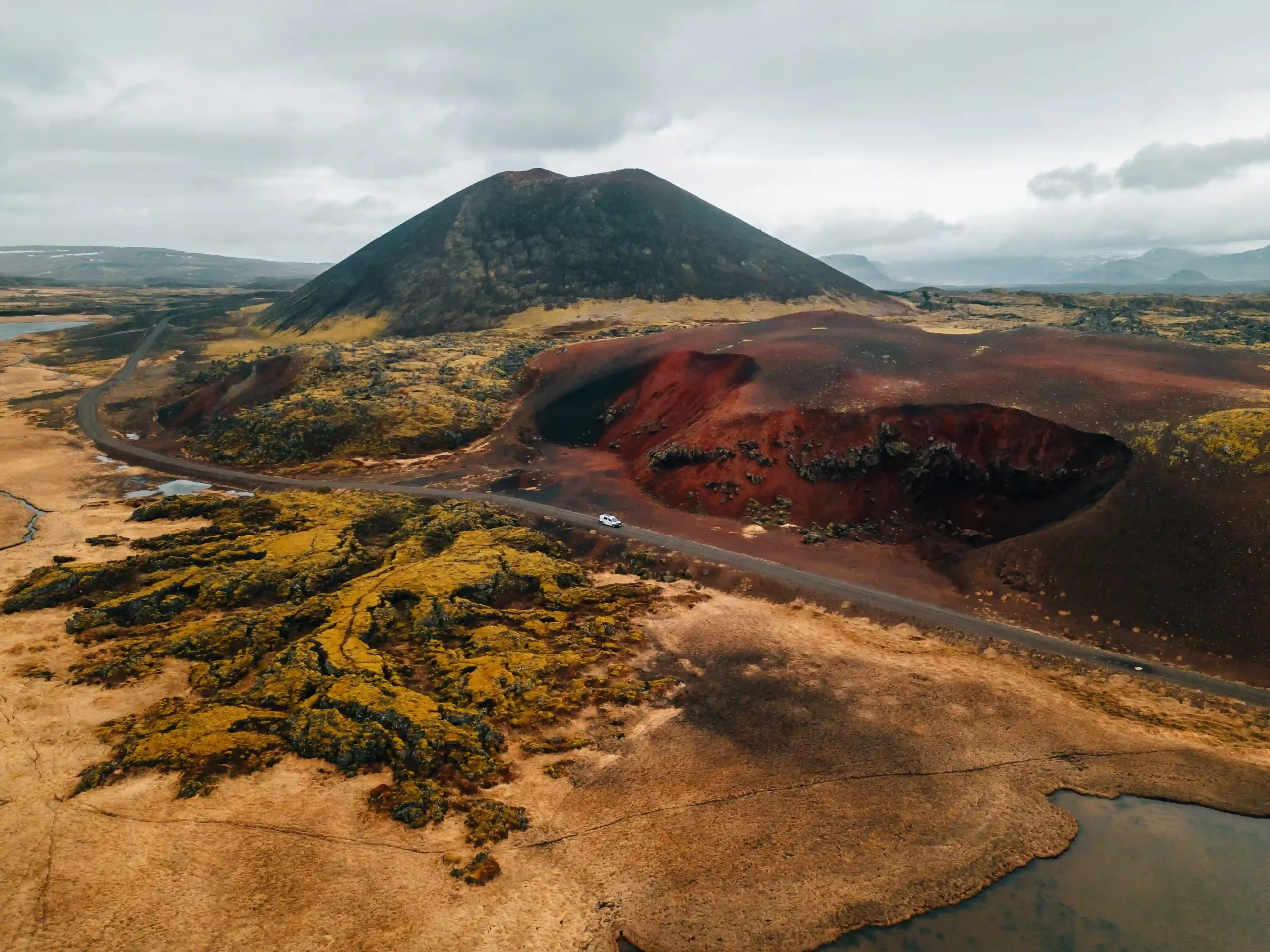 Vibrant red and yellow clay earth contrasts sharply with patches of bright green moss and black volcanic rock under a cloudy sky.