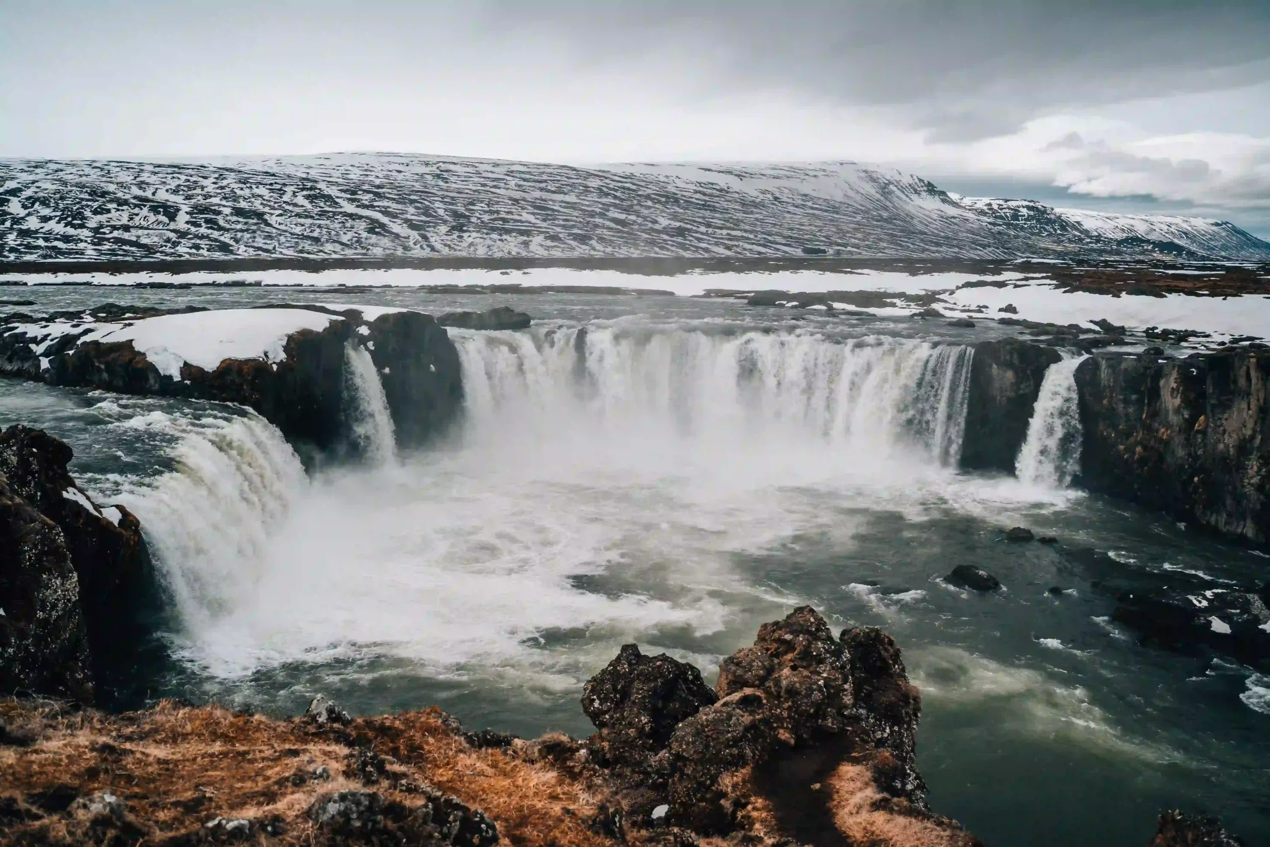 Horseshoe-shaped Goðafoss waterfall plunging into a churning river.