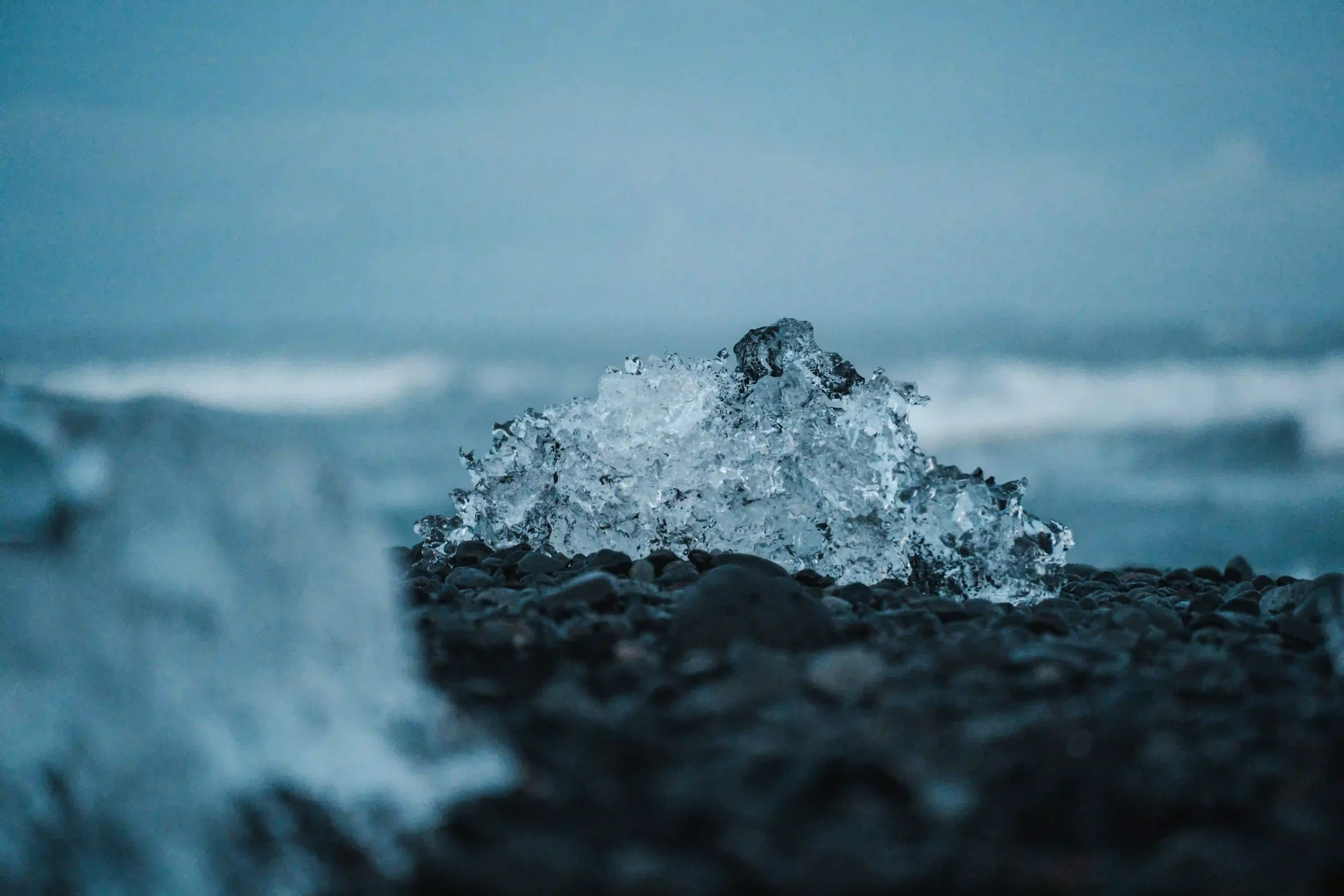 Close-up of a clear, jagged iceberg fragment resting on dark black volcanic pebbles at Diamond Beach.