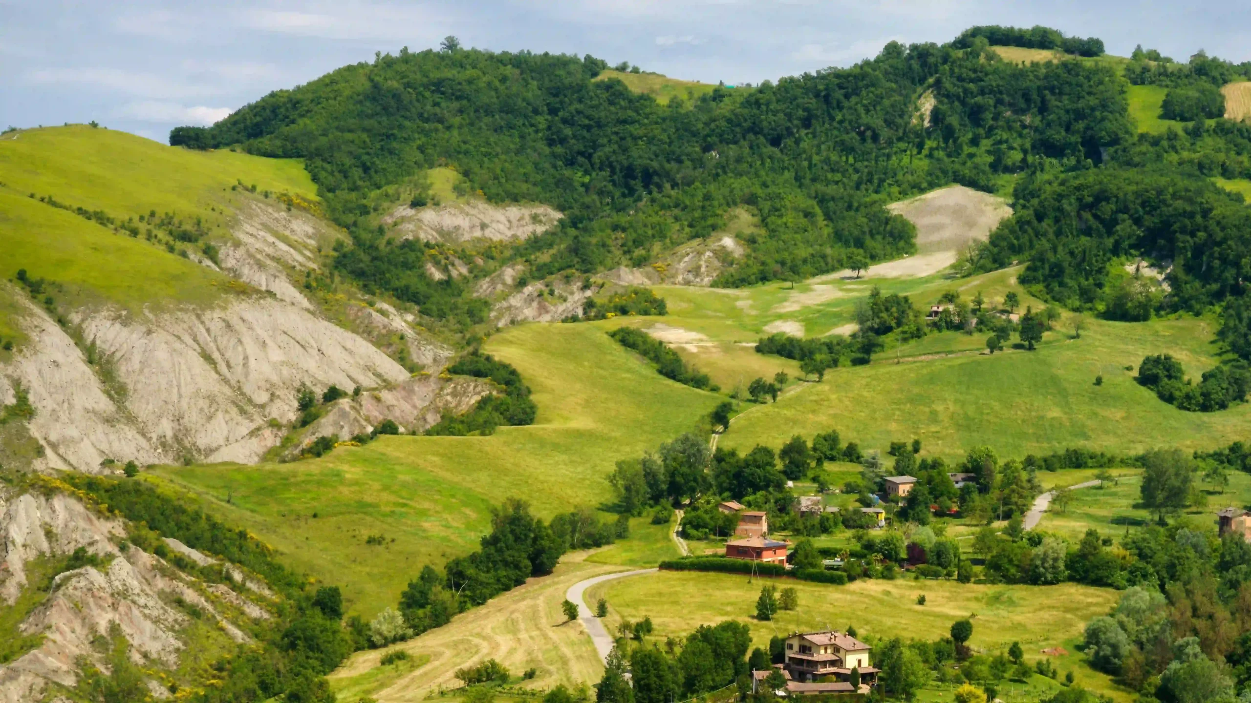 High-angle landscape view of a small rural Italian village nestled among vibrant green rolling hills.