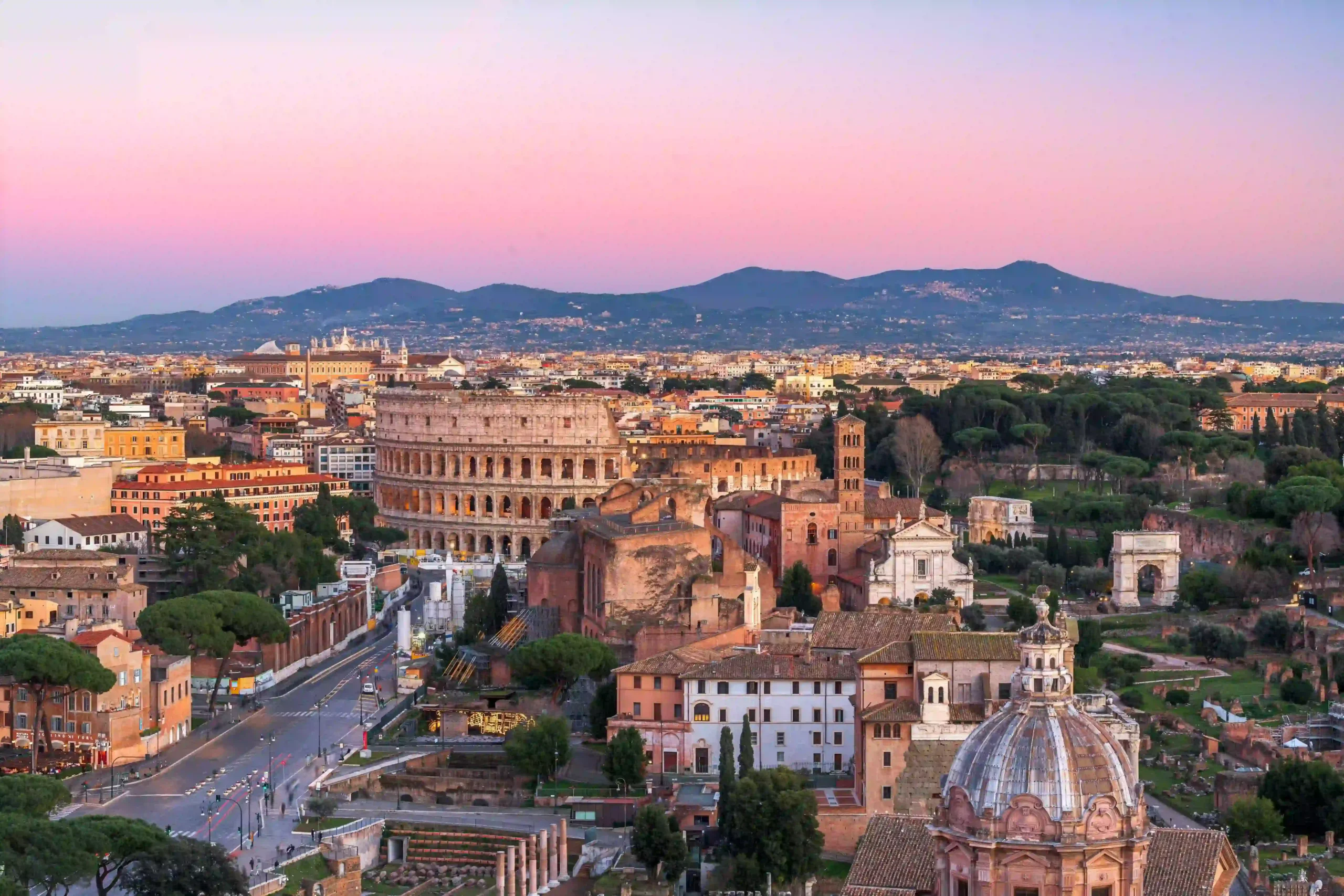 High-angle panoramic view of ancient Rome featuring the Colosseum and Roman Forum ruins.