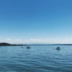 Wide view of Lake Constance on a bright sunny day with several motorboats and the Alps in the distance.
