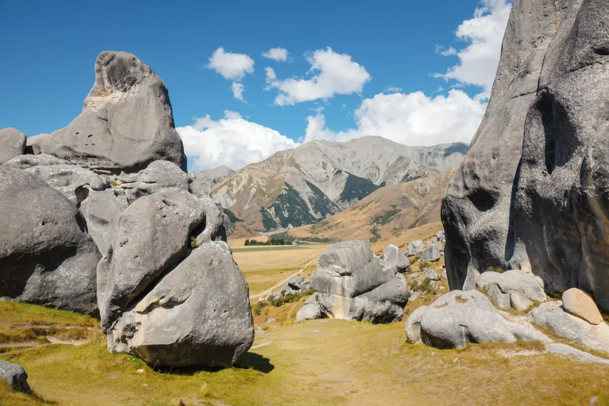 Large, weathered grey limestone rock formations standing in a grassy field with golden hills and a blue sky in the background.