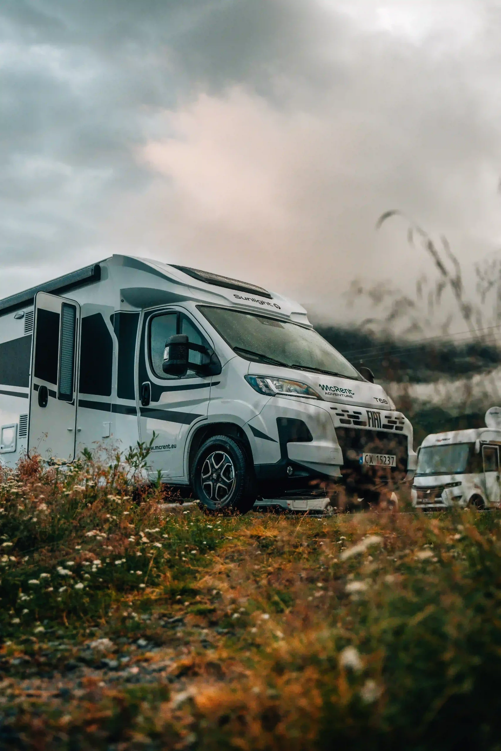 A low-angle, vertical shot of a white a motorhome parked on a grassy, rocky field.