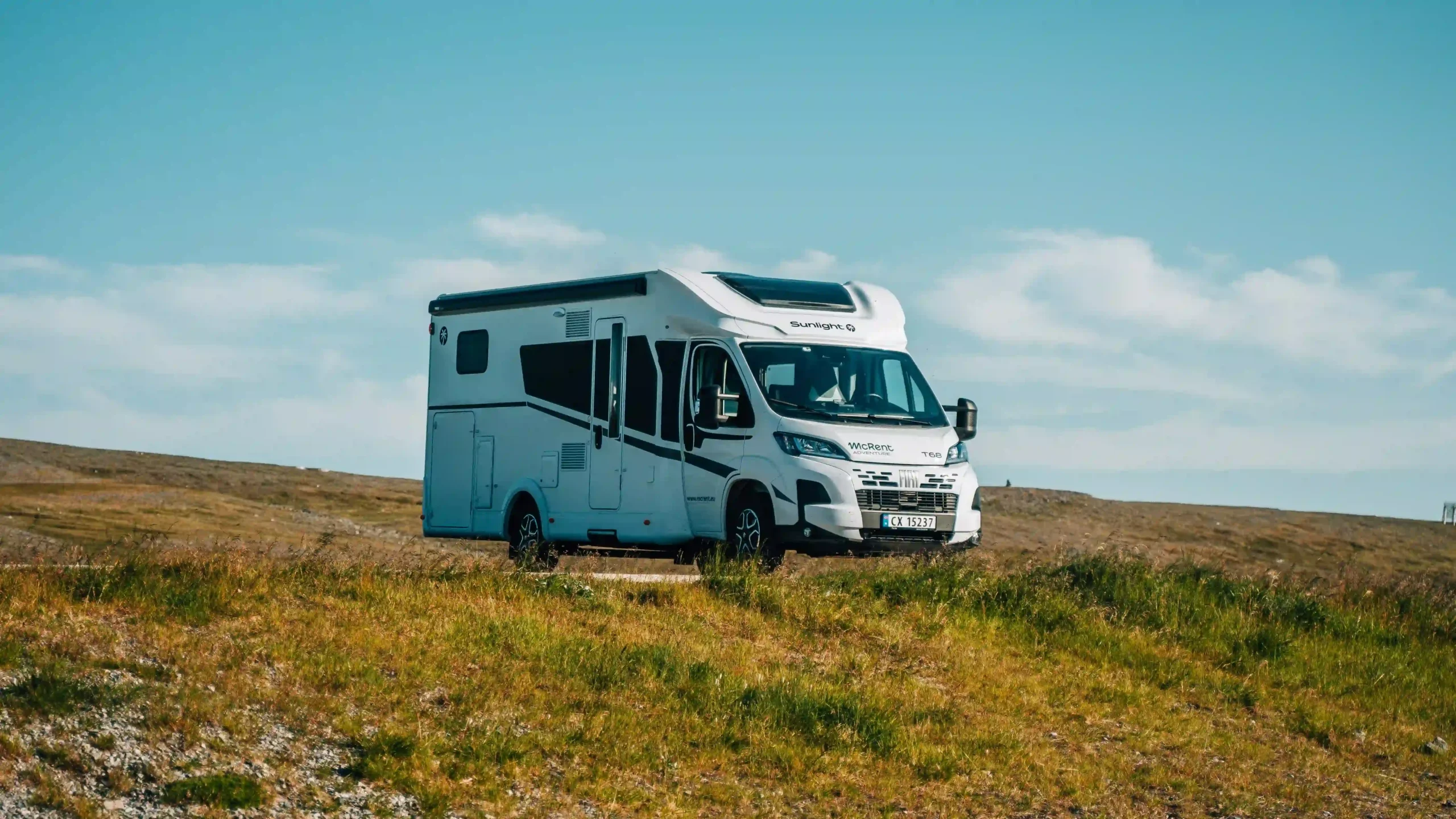 A white campervan parked up on a grassy hill under a vast, bright blue sky.