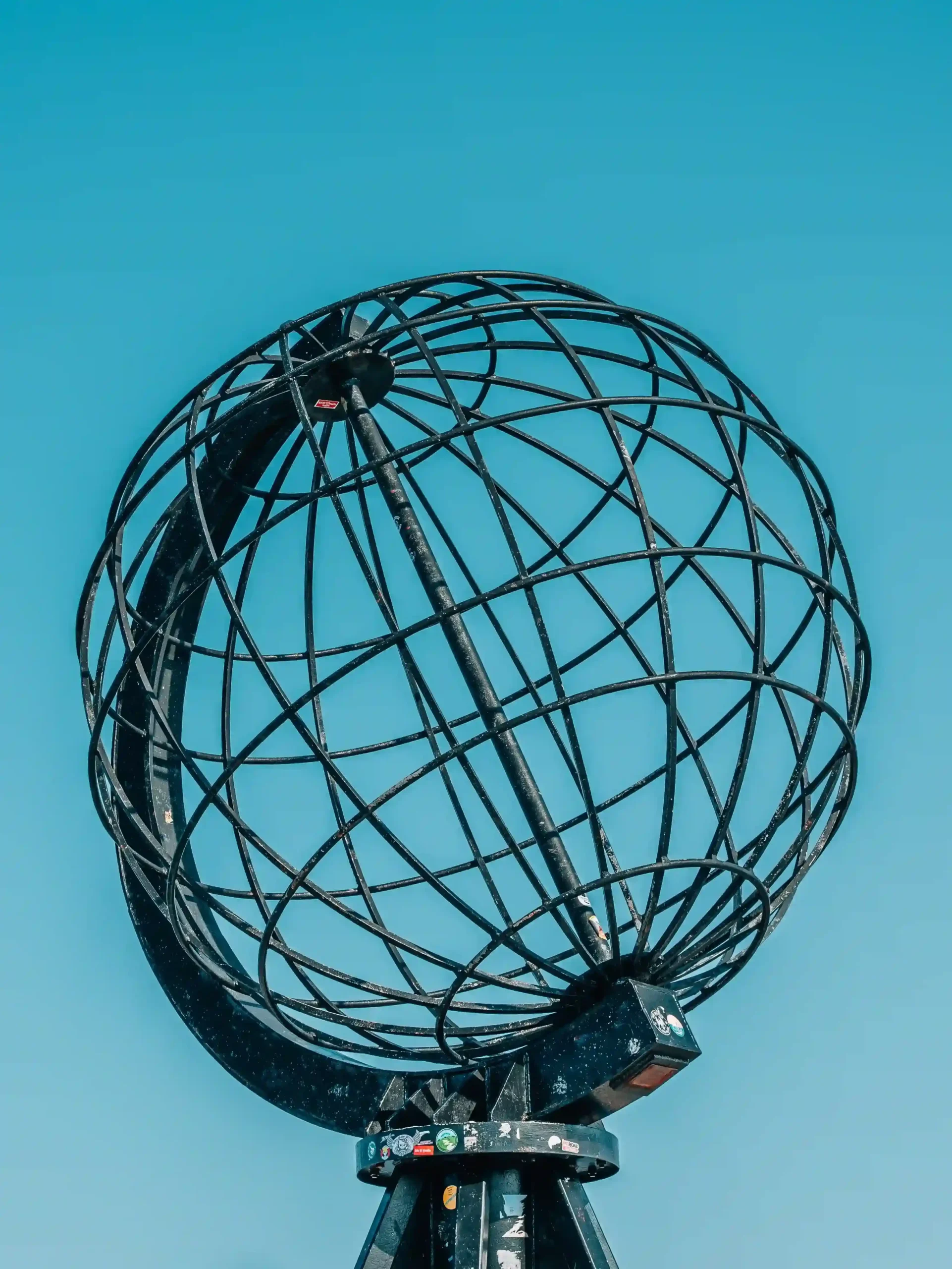 Close-up shot of the North Cape Globe monument, a large black steel wireframe globe, set against a vibrant, blue sky.
