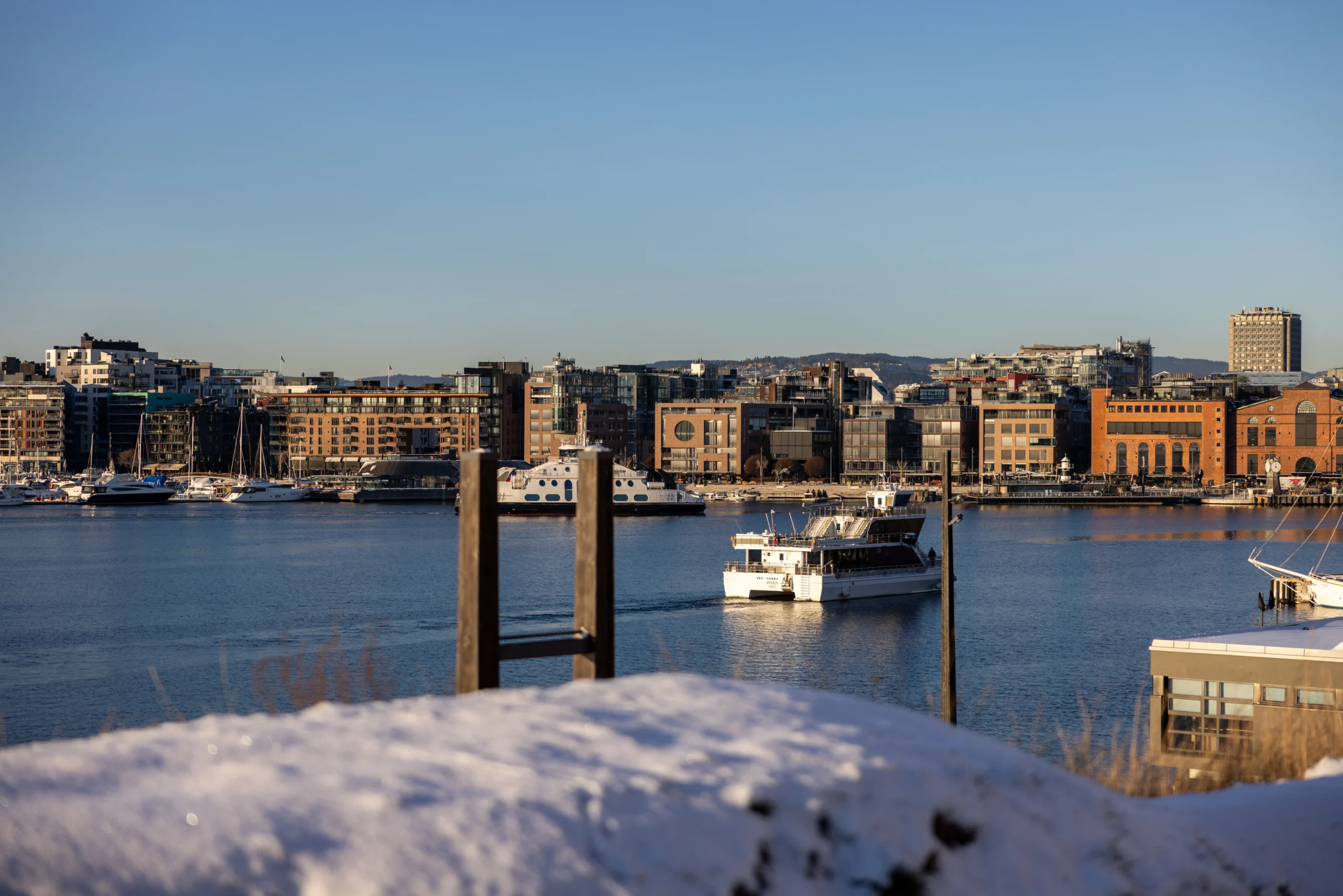 A wide shot of the Oslo waterfront in winter featuring modern apartment buildings and white passenger ferries.