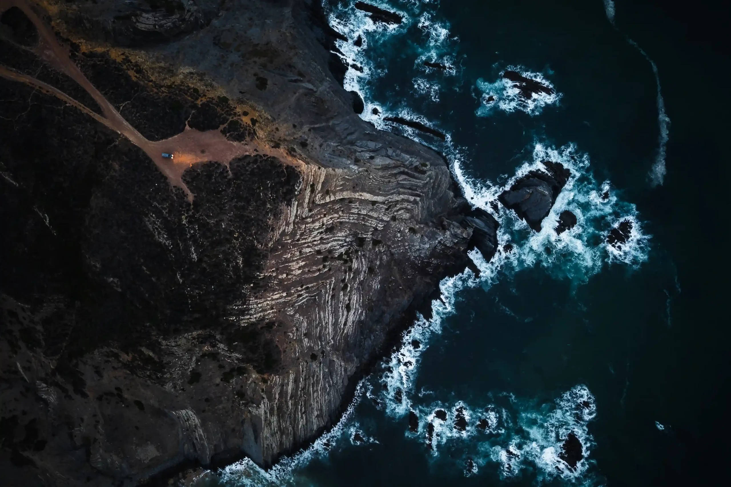 Powerful white sea foam and waves crash against the jagged rock formations.