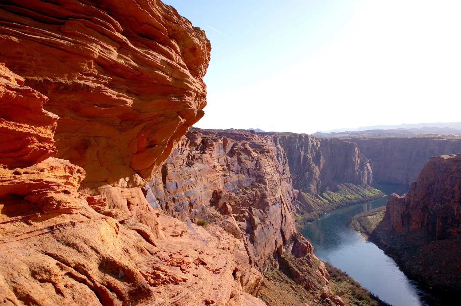 A view looking down from a red rock cliff edge towards the Colorado River winding through the deep canyons of the Grand Canyon below.