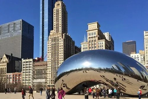 The famous Cloud Gate sculpture (The Bean) in Chicago reflecting the city skyline and blue sky on a sunny day.