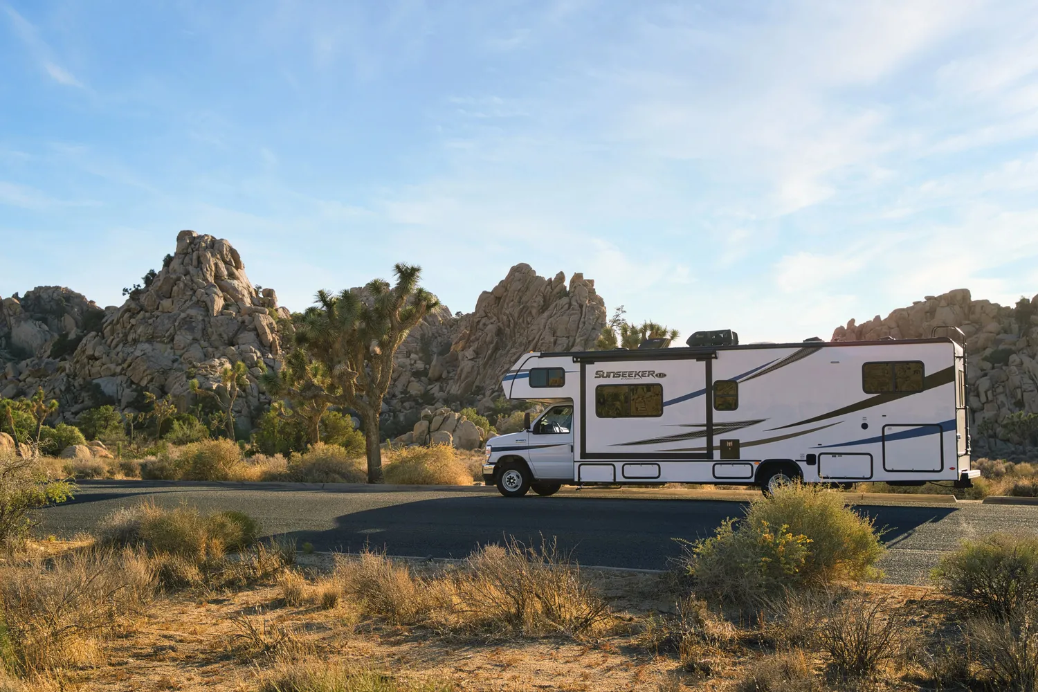 A large white El Monte RV driving on a desert road.