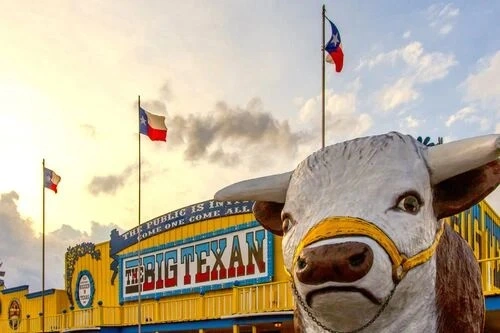 A close-up of a large statue of a bull in front of The Big Texan Steak Ranch building.