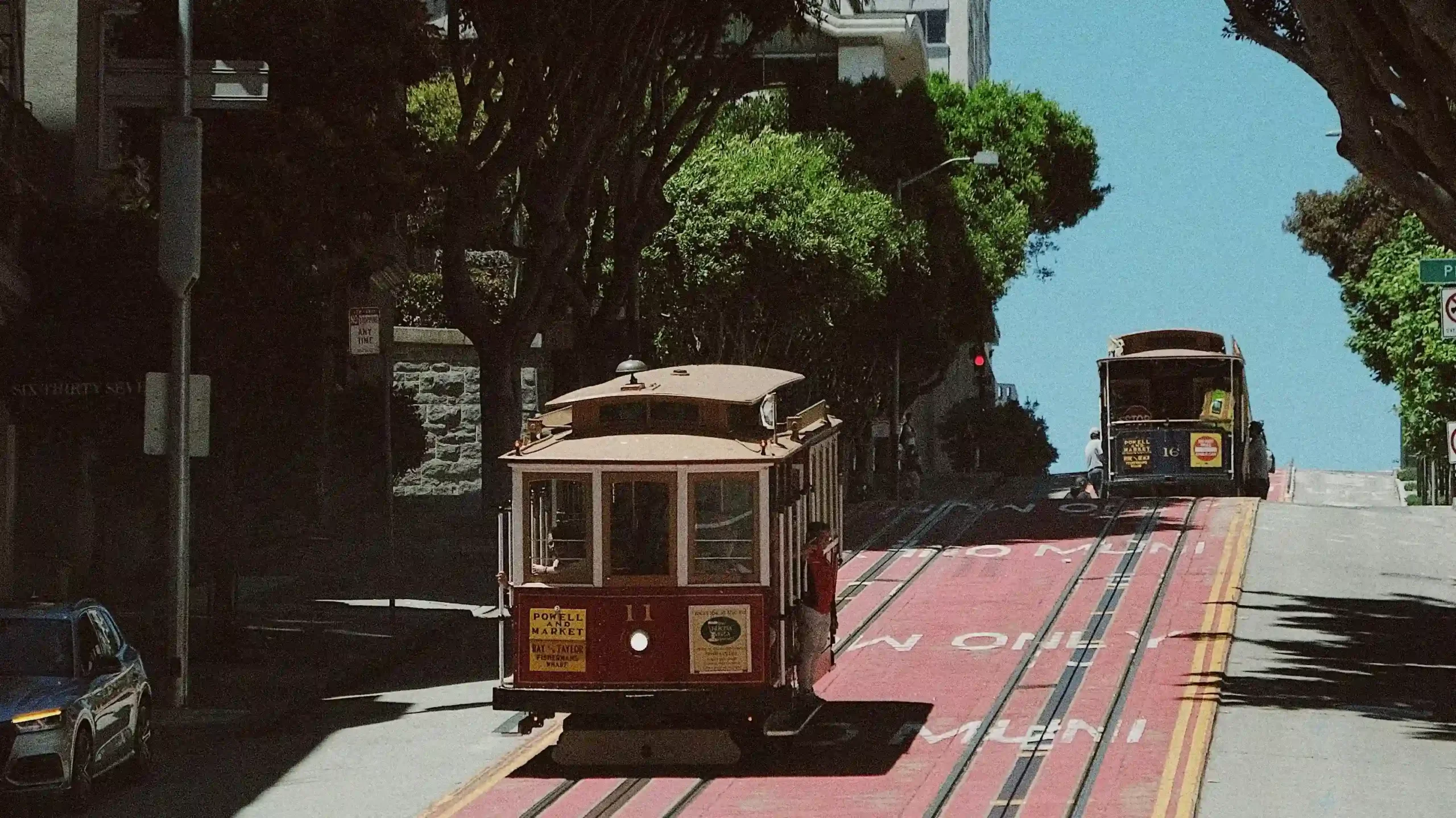 San Francisco cable car riding along a tree-lined street hill.