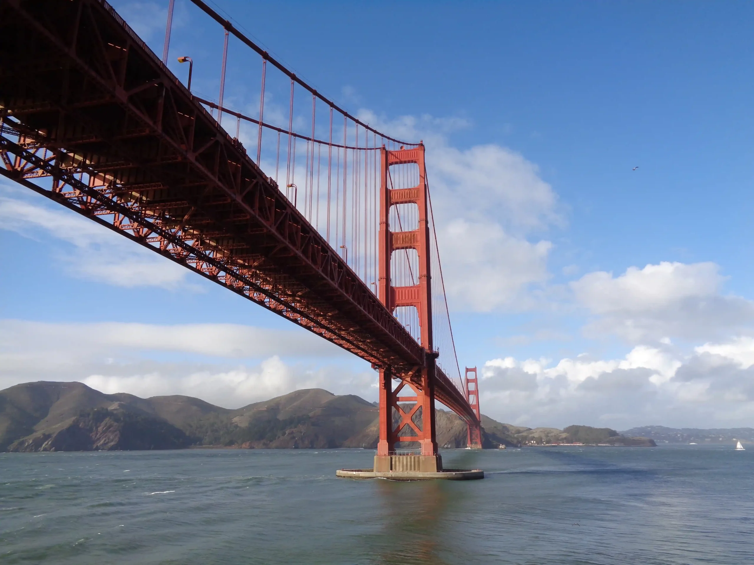 Looking up at the orange-red suspension cables and towers of the Golden Gate Bridge.