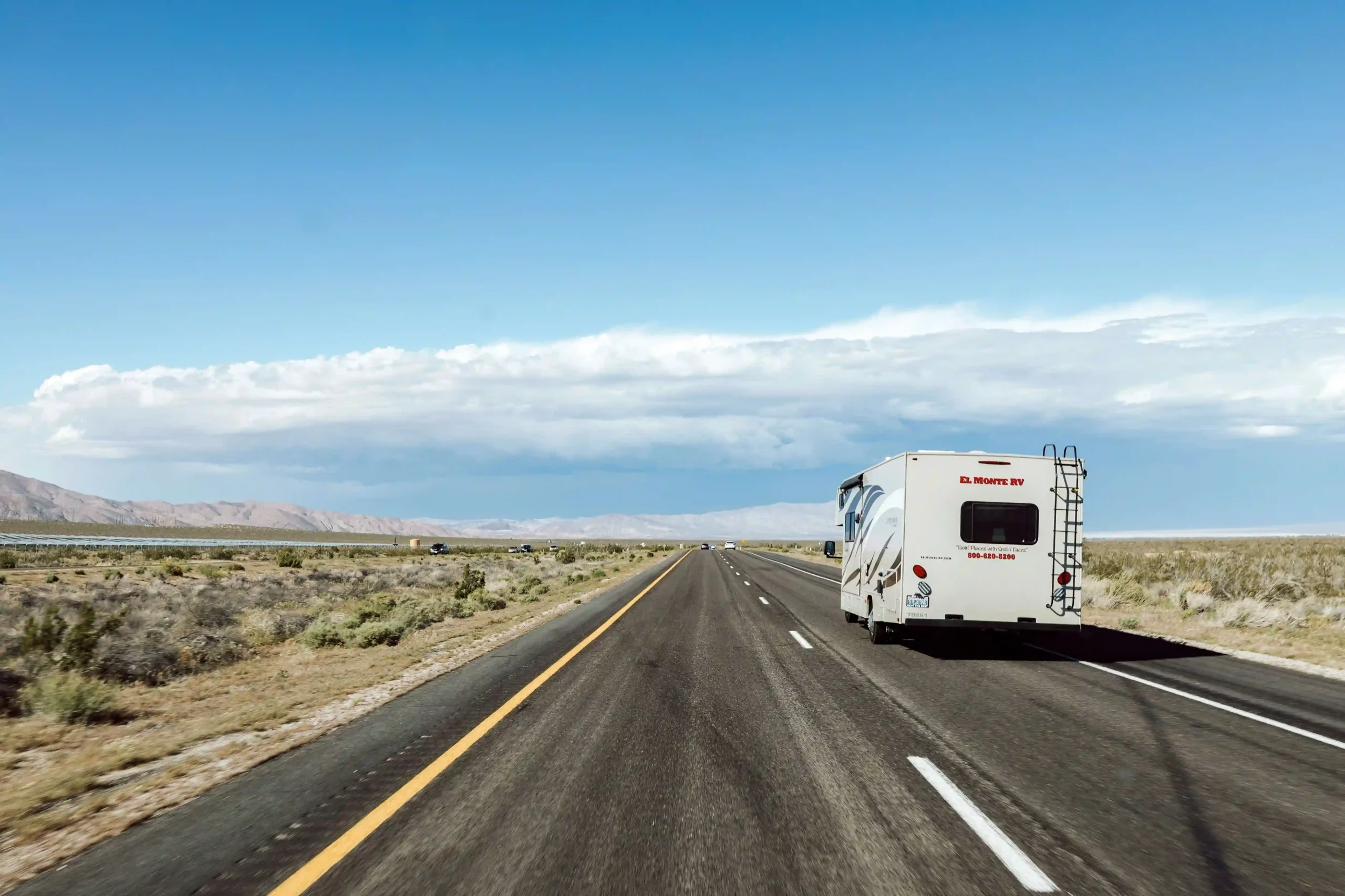 White RV driving through a desert on a run-of-fleet transfer route, with distant mountains.
