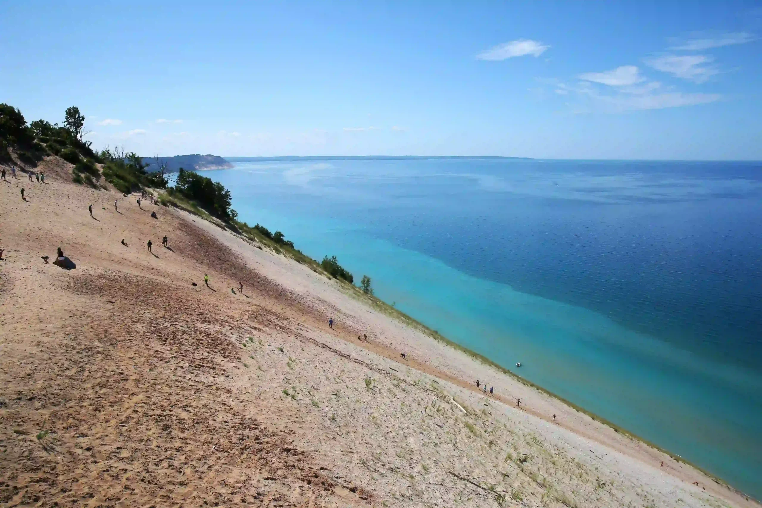 View of a steep sand dune sloping down into the vibrant turquoise and deep blue waters of Lake Michigan.