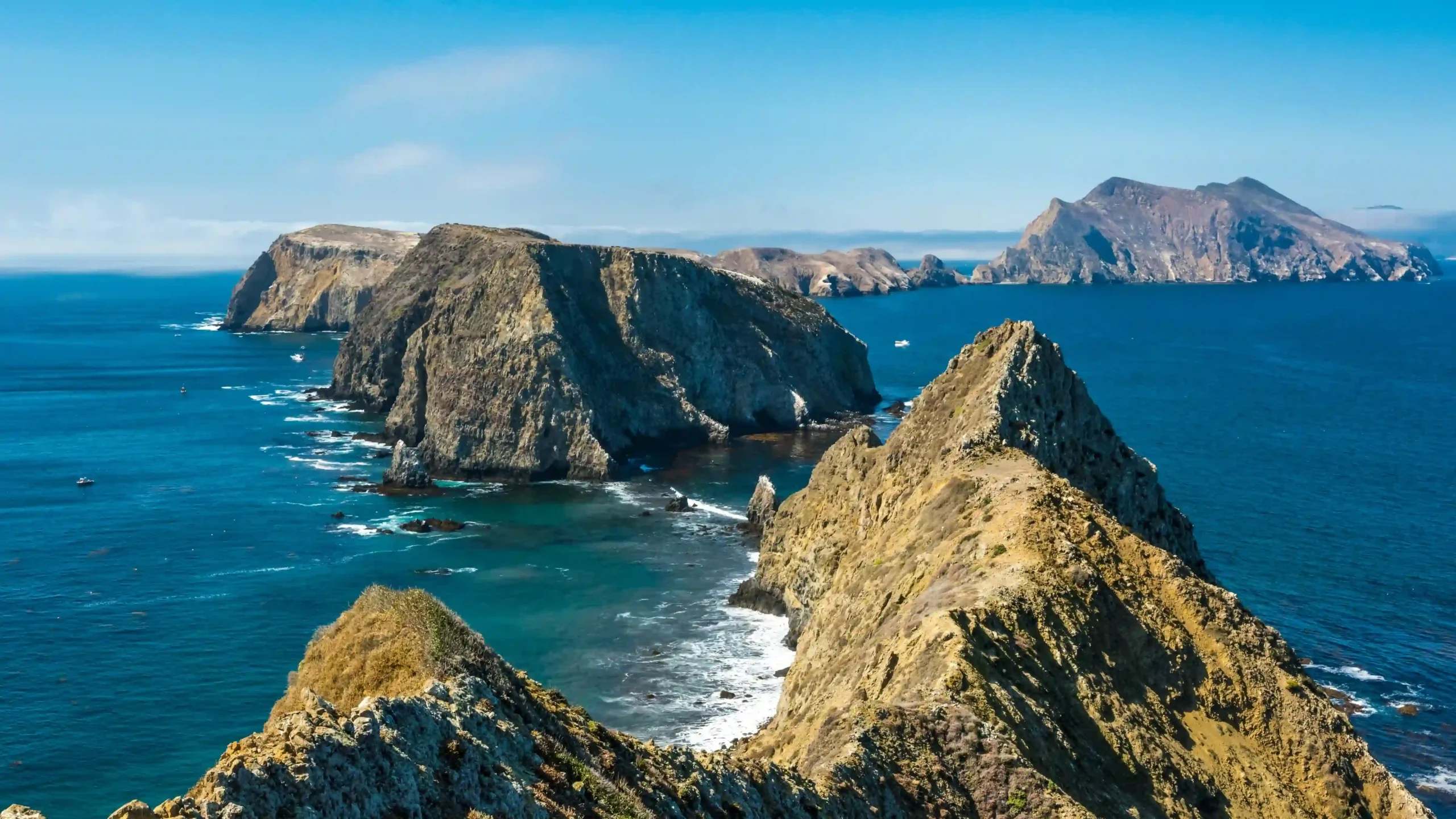 A high-angle, scenic view looking down a sharp, rugged rocky ridge of Anacapa Island as it breaks into smaller islet chains extending into a vibrant blue Pacific Ocean under a clear sky.