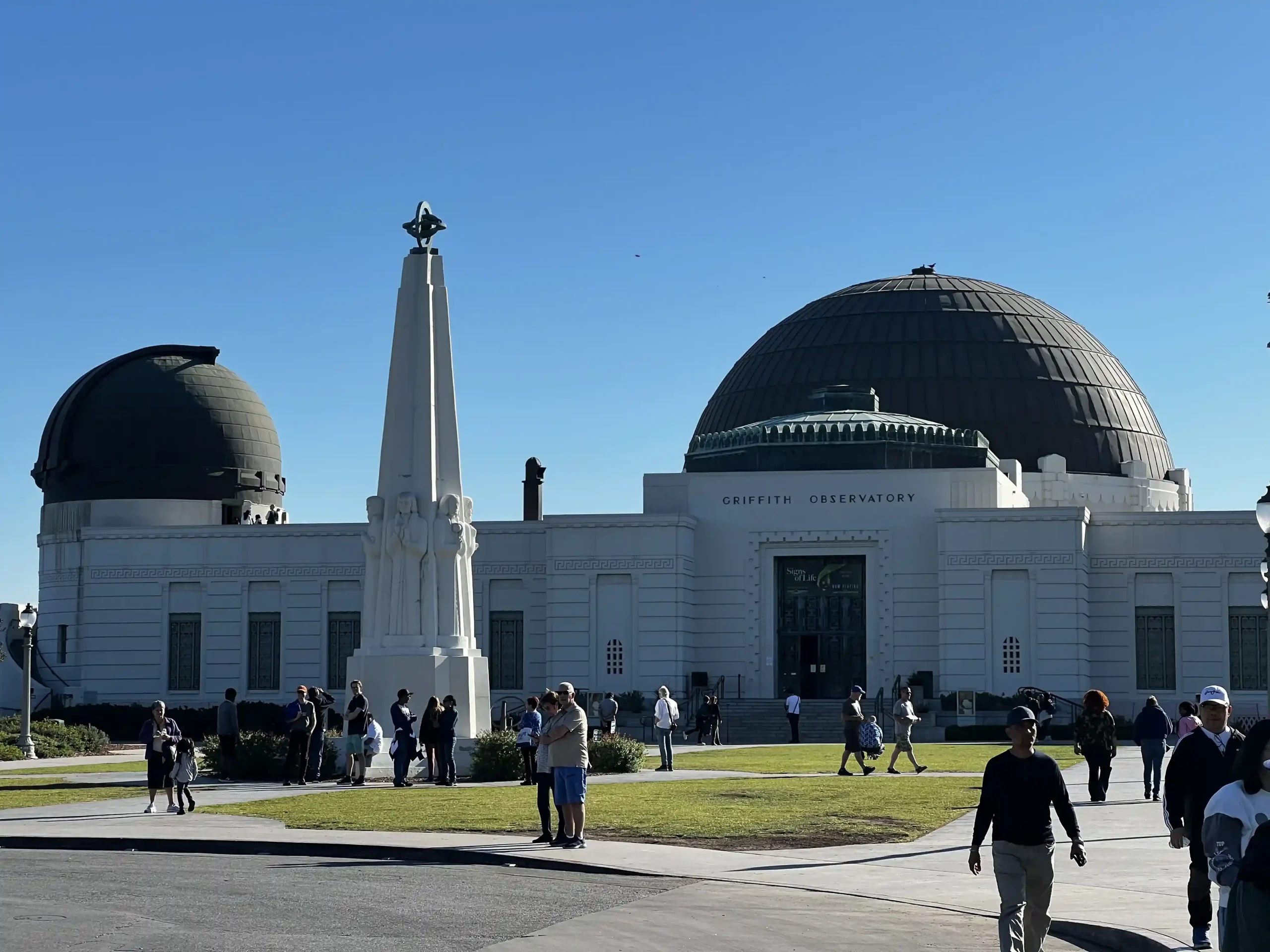View of the Griffith Observatory in Los Angeles on a bright, sunny day. The white building features its central copper dome and a smaller telescope dome to the left.