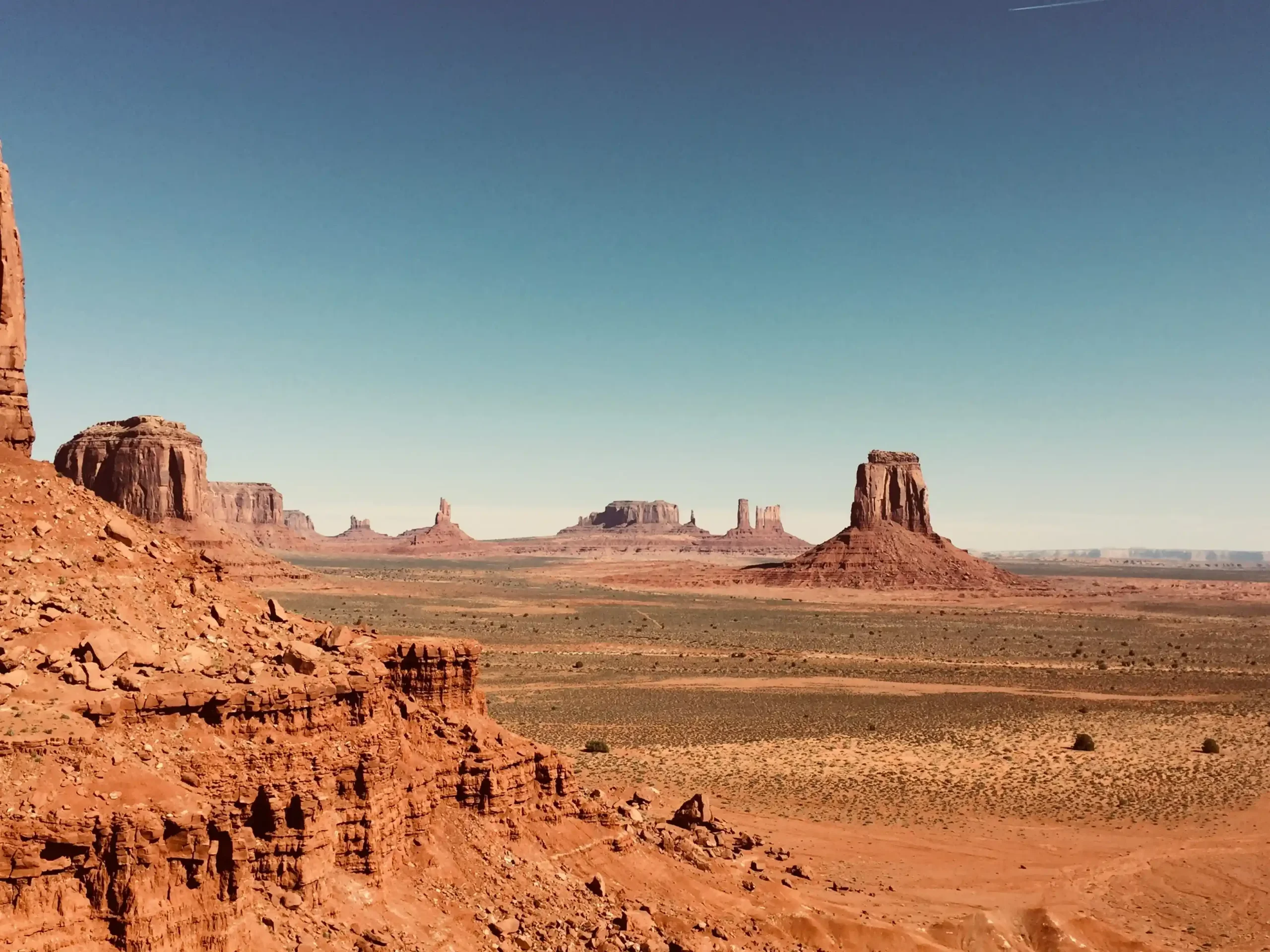 An elevated, wide-angle view of the Monument Valley desert featuring steep red rock cliffs.