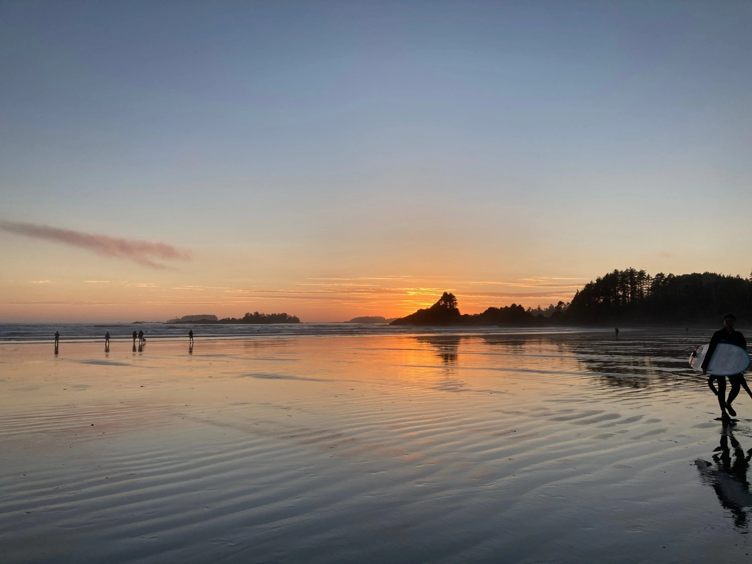 A wide view of a flat, sandy beach at low tide during a vibrant orange and purple sunset.