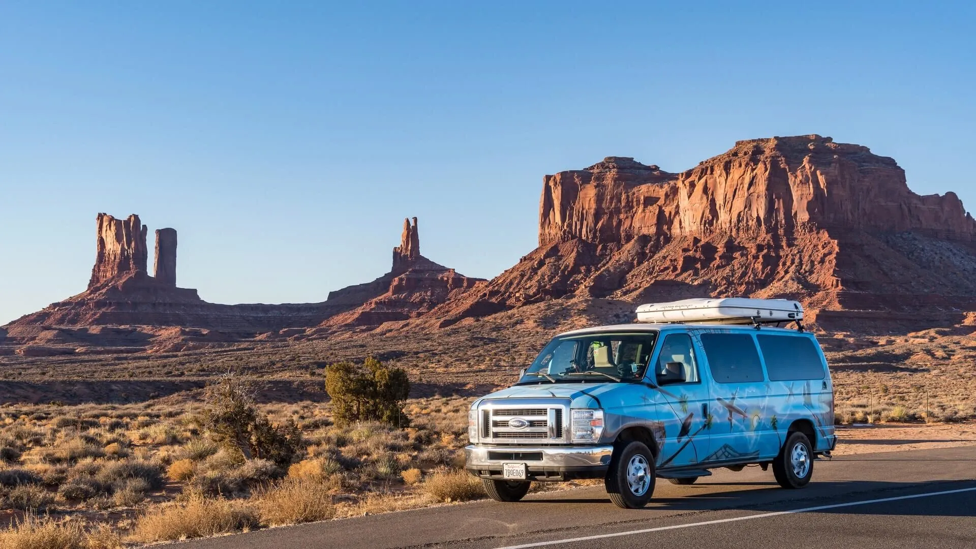 Un camping-car du loueur Escape roule sur une route désertique de l\'Utah avec des formations rocheuses en arrière-plan.