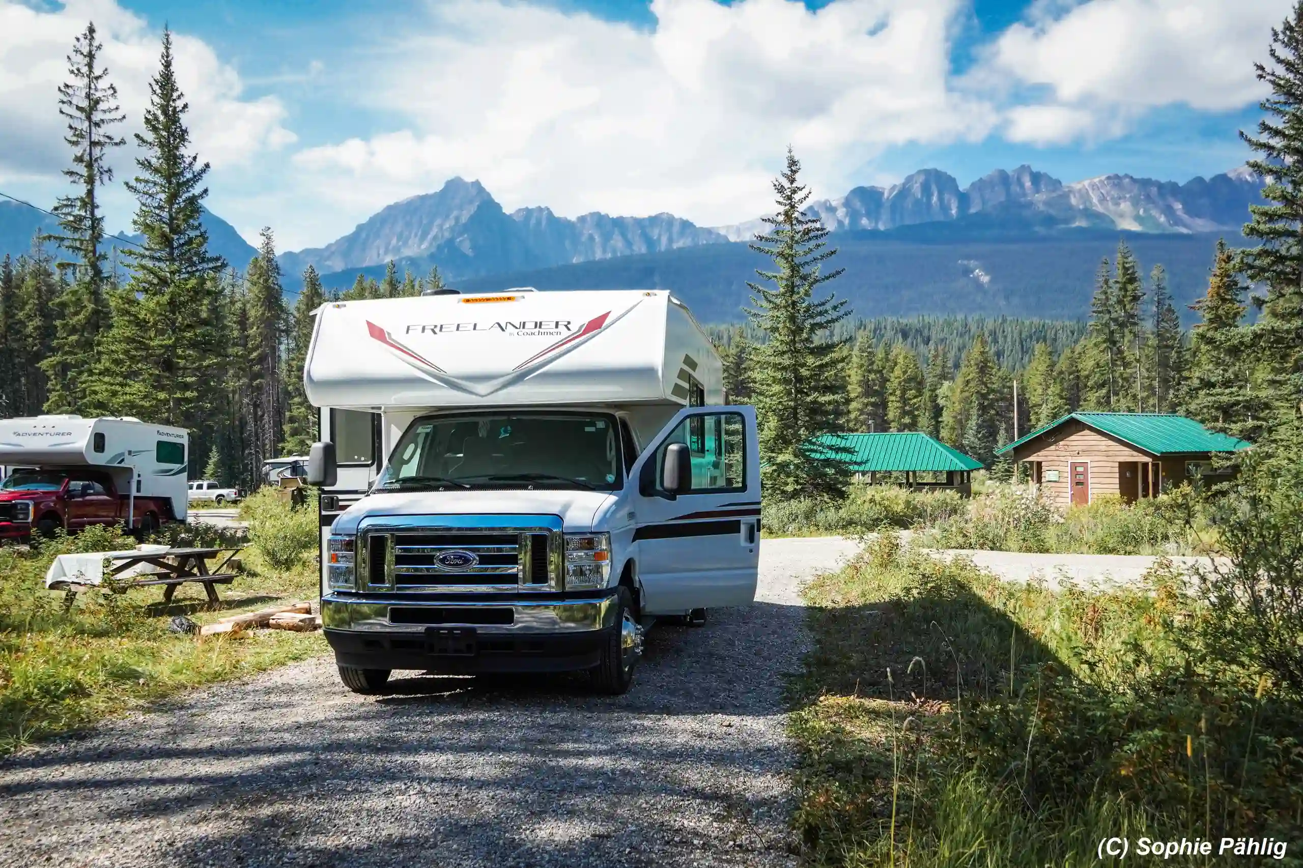 Un camping-car loué au Canada est garé sur un terrain entouré d'arbres et de massifs montagneux.