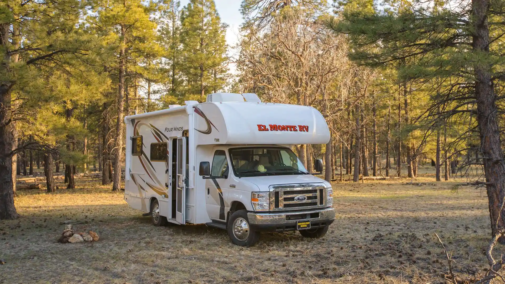 Un camping-car El Monte RV pour une location de camping-car aux USA sur un camping ou une place de parking, devant une forêt