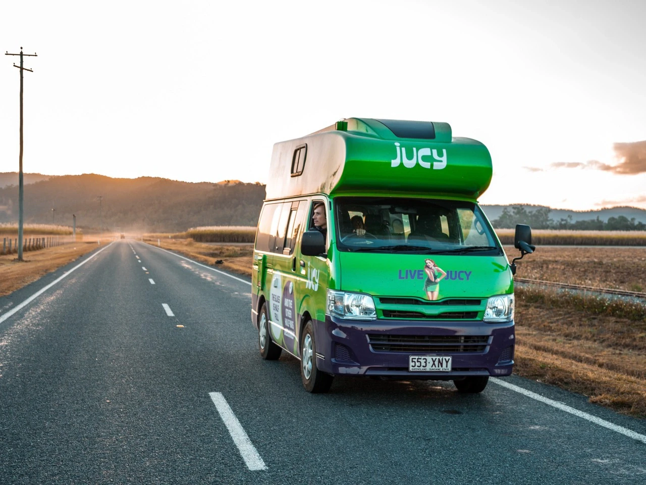 Un van aménagé de la marque Jucy roule sur une route australienne.